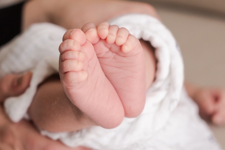 Close-up of newborn baby feet wrapped in a white swaddle blanket during an in-home newborn photography session in Grand Rapids Michigan — Jules K Photography