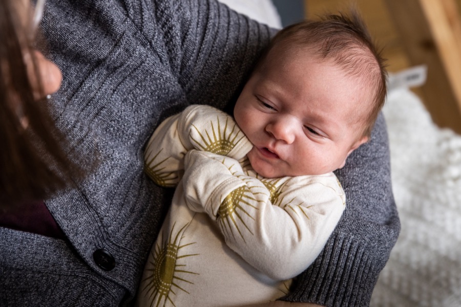 Sleeping newborn baby in a sun-print onesie being held by mom during an in-home newborn photography session in Grand Rapids Michigan — Jules K Photography