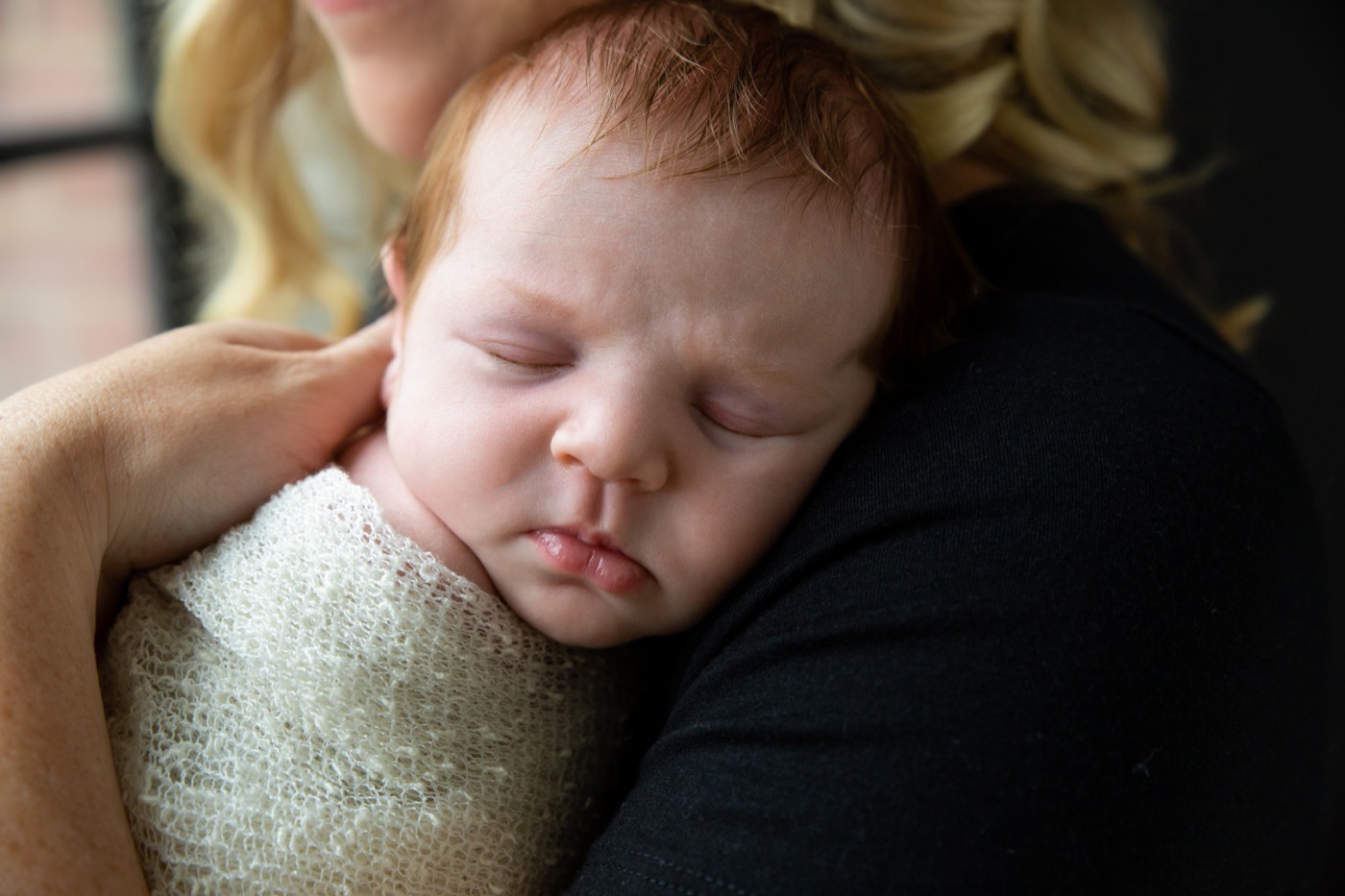 Sleeping swaddled newborn baby with red hair resting on a parent's shoulder during an in-home newborn photography session in Grand Rapids Michigan — Jules K Photography
