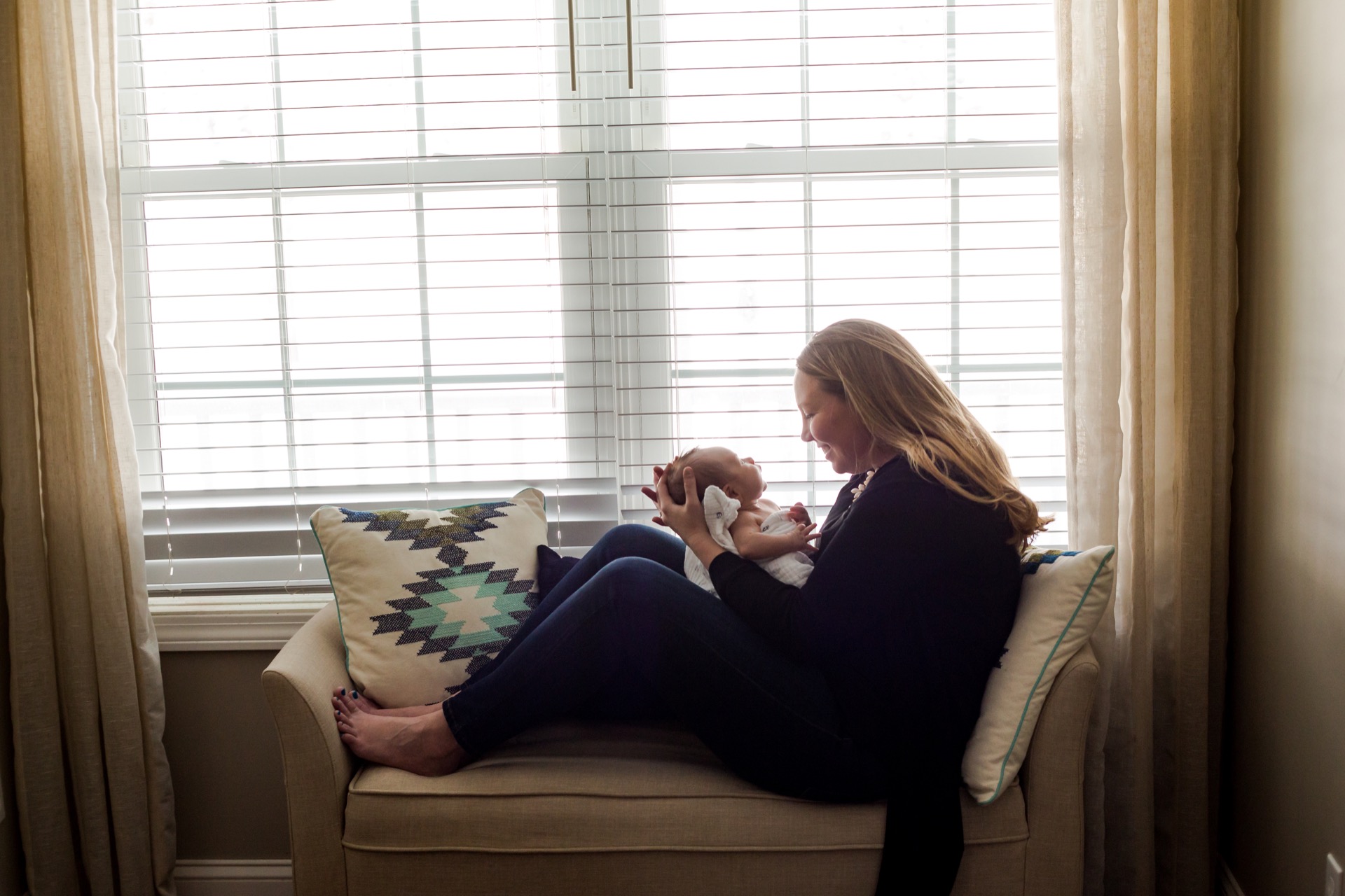 Mom with newborn by window in-home session Michigan