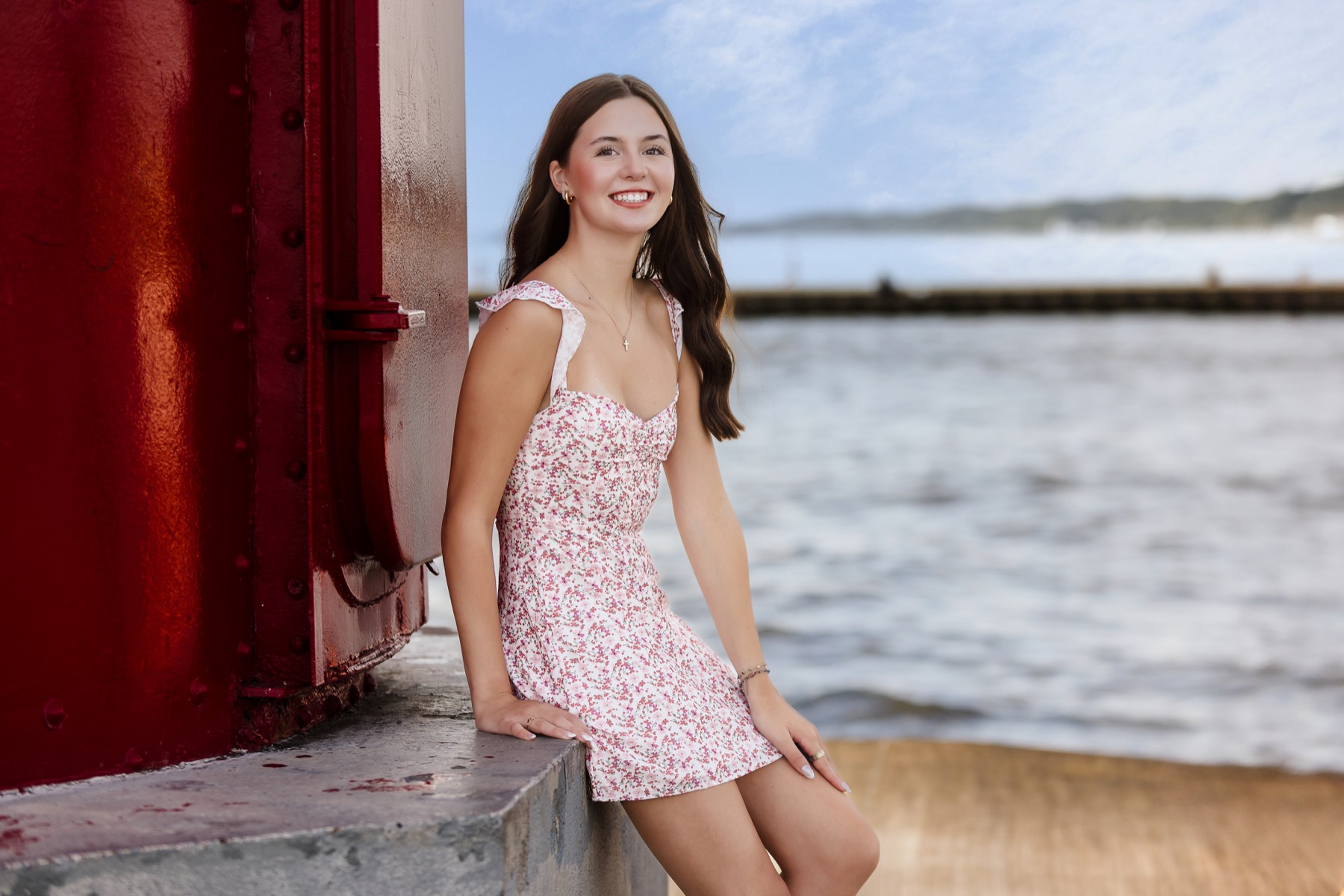 High school senior girl sitting near the Grand Haven lighthouse and pier on Lake Michigan