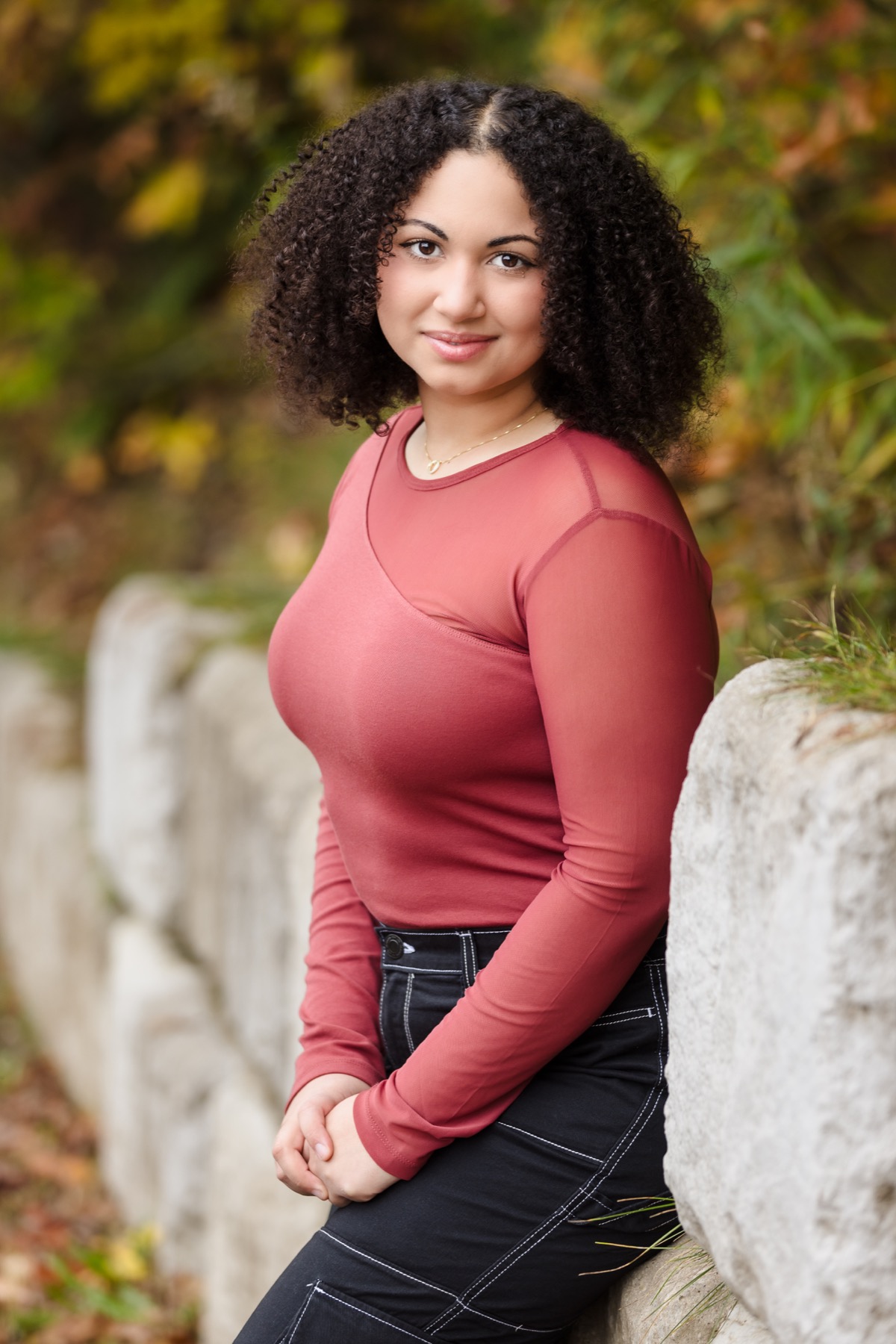 High school senior girl leaning against stone wall with fall foliage at Grand Ravines Park in Jenison Michigan