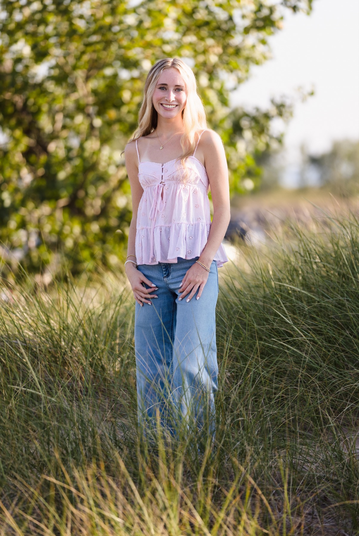 High school senior girl standing in Lake Michigan sand dunes with tall grasses at golden hour
