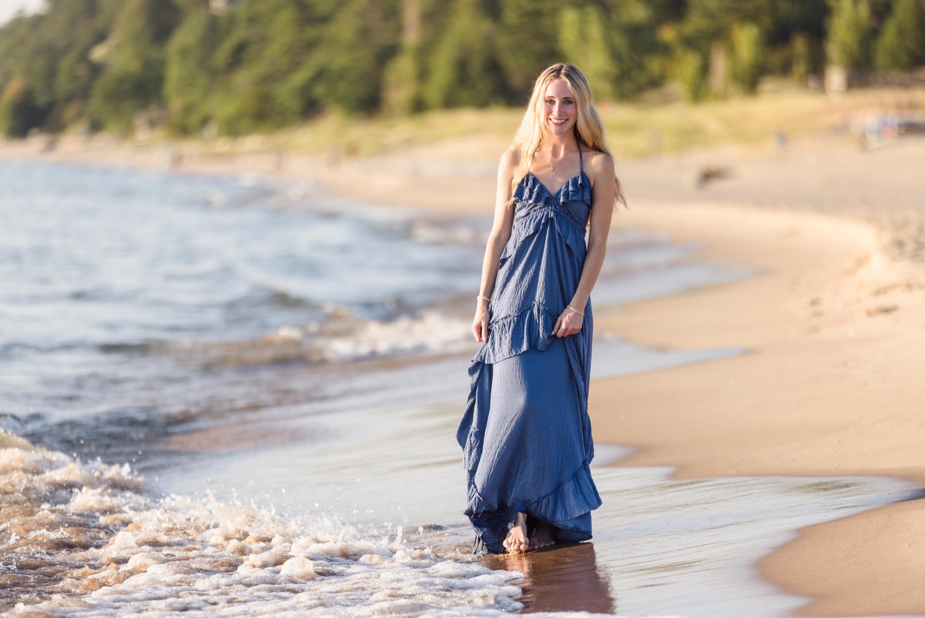 High school senior girl in blue dress walking along the Lake Michigan shoreline at golden hour